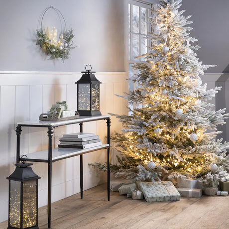 Decorated Christmas tree with lights and presents in a room with a console table and lanterns.